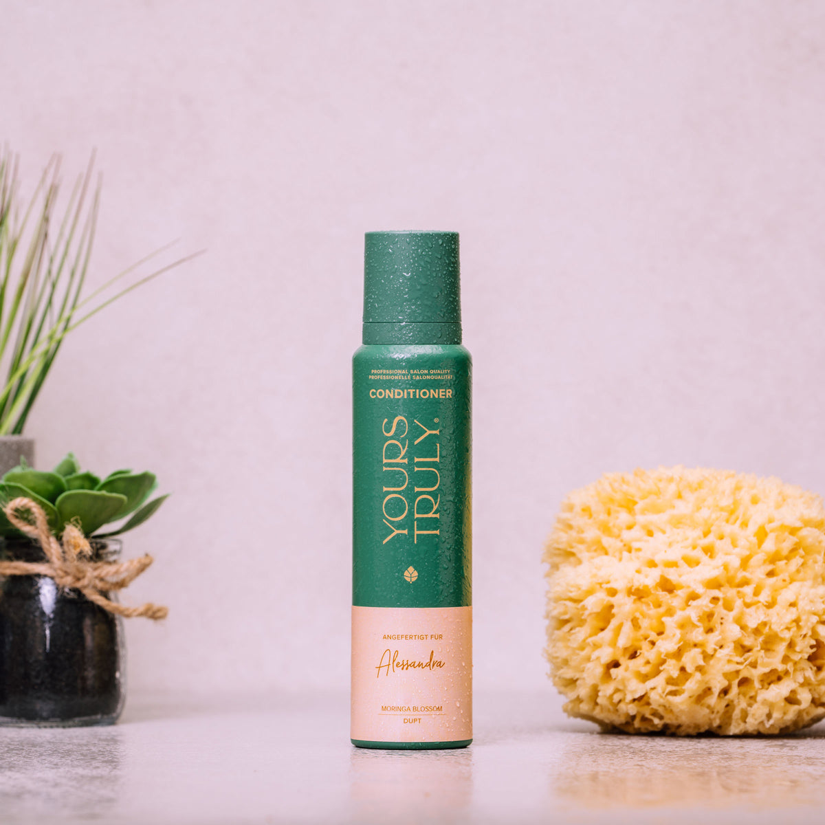 yours-truly-conditioner-flasche-mit-namensetikett-und-wassertropfen-neben-pflanzen-und-gelb-schwamm-im-badezimmer