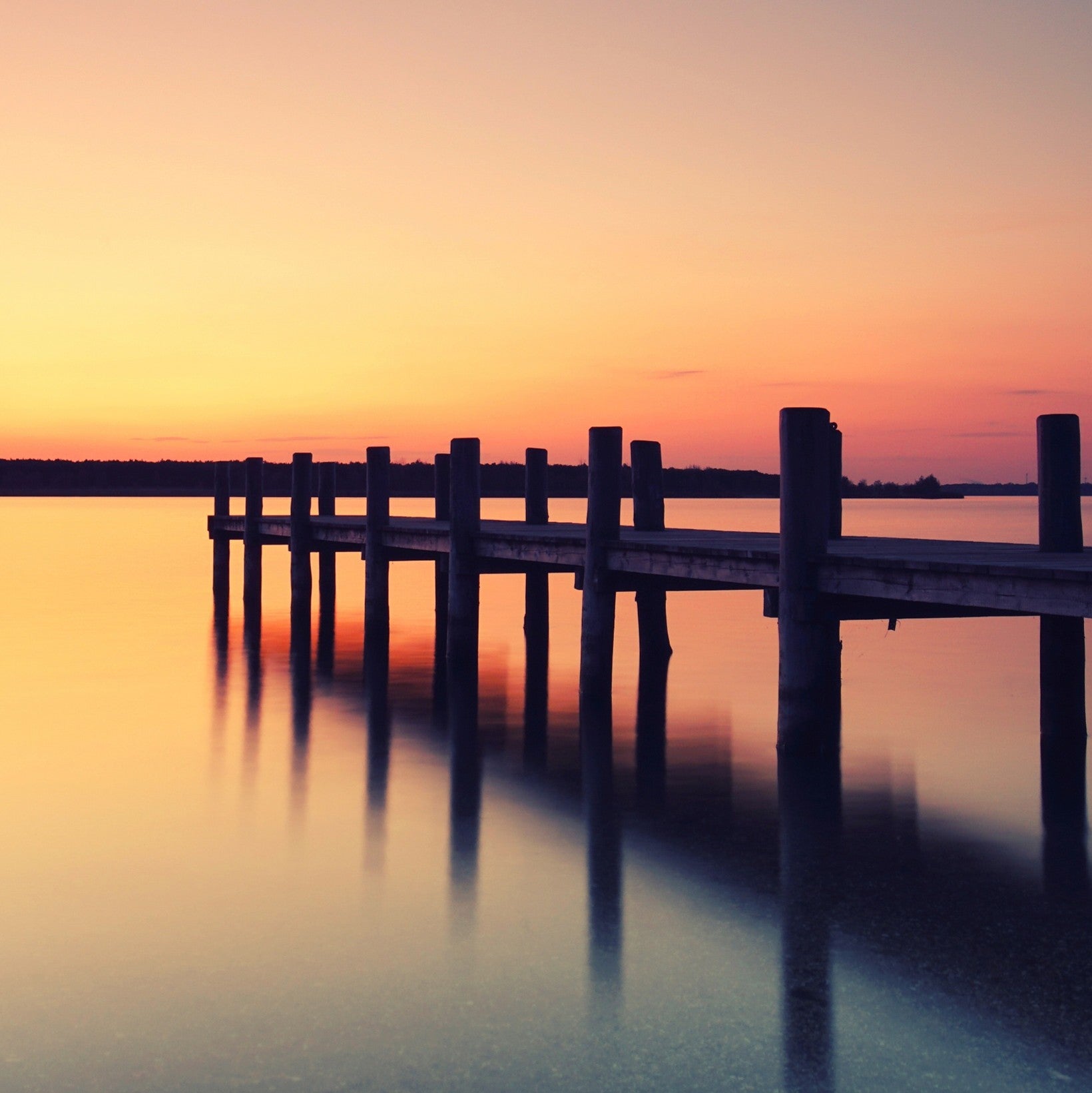 holzsteg-am-see-im-sonnenuntergang-mit-spiegelung-im-wasser