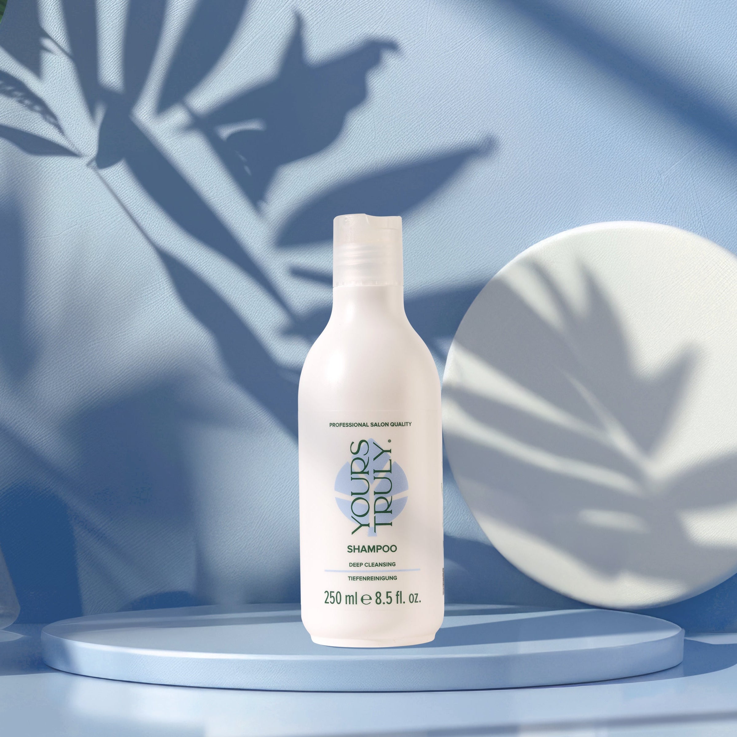 yours-truly-deep-cleansing-shampoo-in-weißer-250ml-flasche-auf-rundem-podest-mit-blauem-hintergrund-und-pflanzenschatten